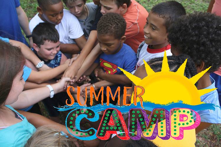 Group of diverse kids at summer camp placing their hands together in a team circle, with a colorful "Summer Camp" graphic overlay.
